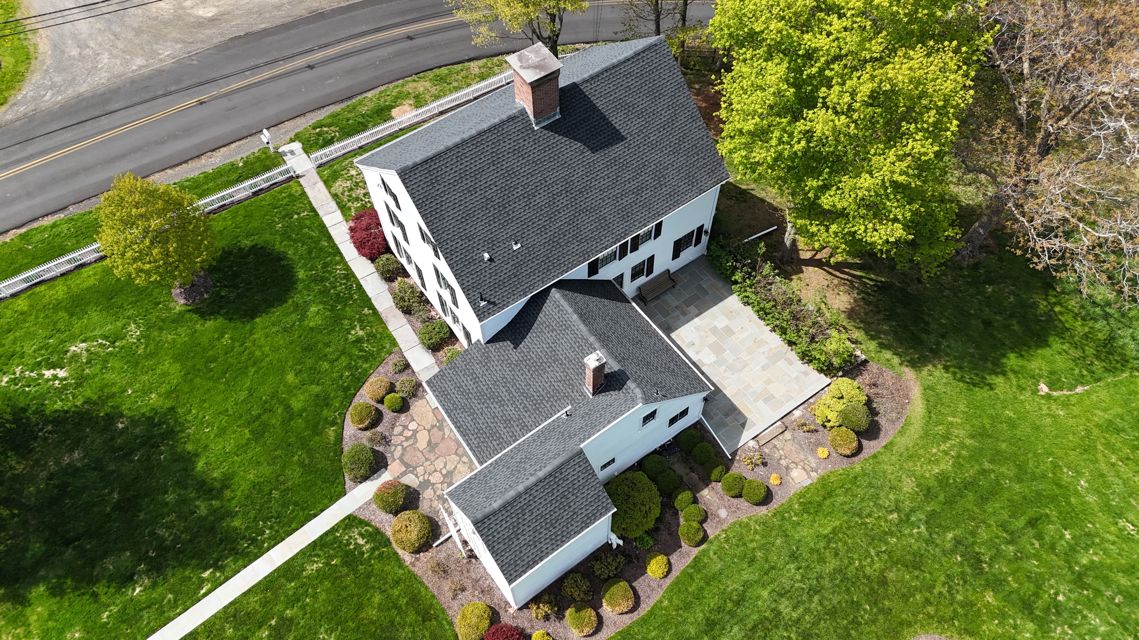 Aerial view of a finished Pattison Construction home in Connecticut — white siding, dark shingle roof, paver patio, landscaped grounds