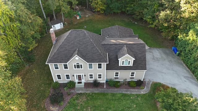 Pattison Construction finished roof on a beige-siding colonial set into a wooded Connecticut lot — aerial view