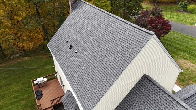 Pattison Construction crew installing a new asphalt-shingle roof on a Connecticut home — aerial view with attached deck and autumn foliage